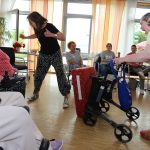 Eine Frau fährt mit dem Rollator gegen das Schutzpolster. Die Frau, die dahinter steht, macht einen Schritt nach hinten.